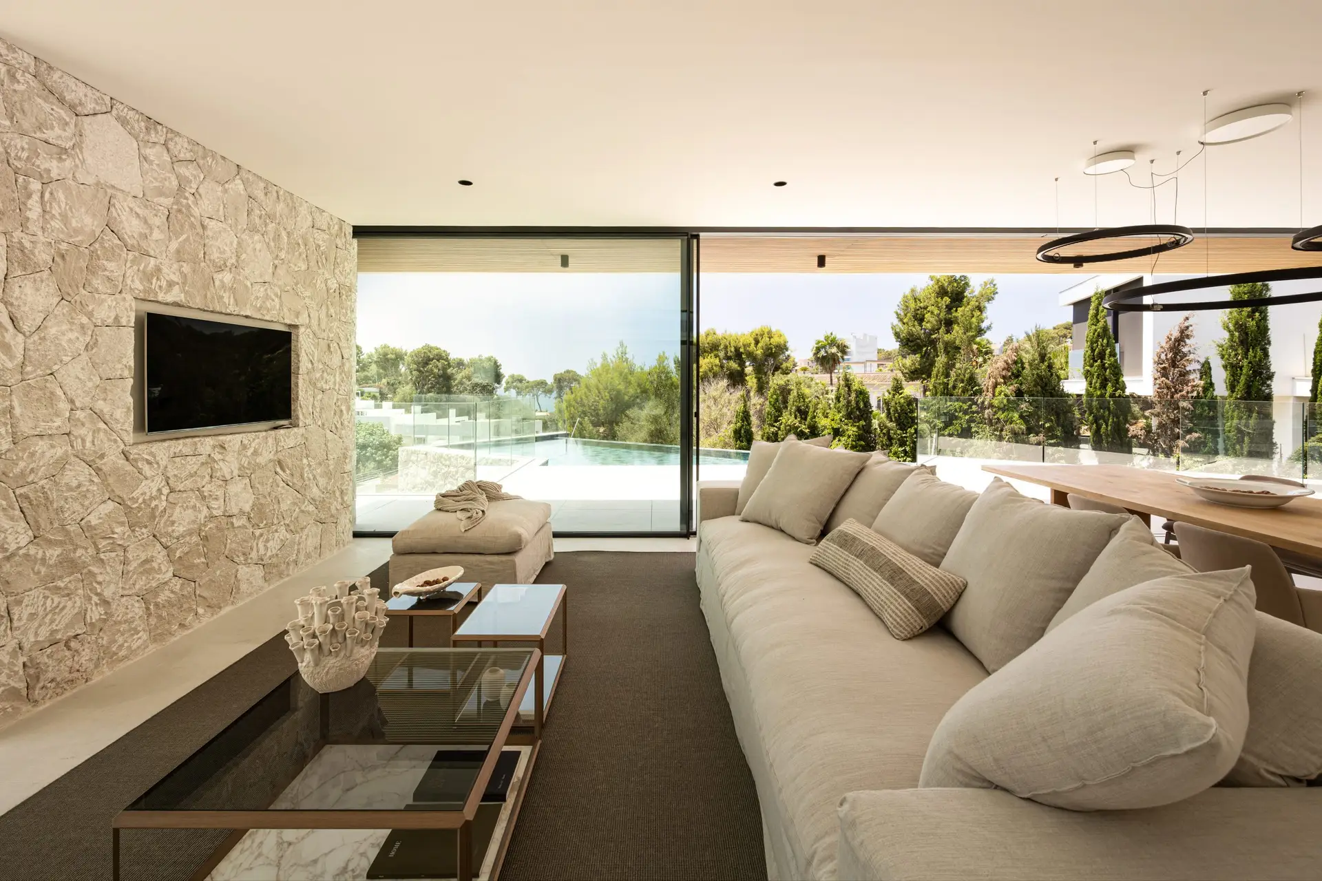 Luxury villa living room with natural stone walls, pool terrace and garden views in Bendinat, Mallorca — exclusive property represented by Isabella Janoschka