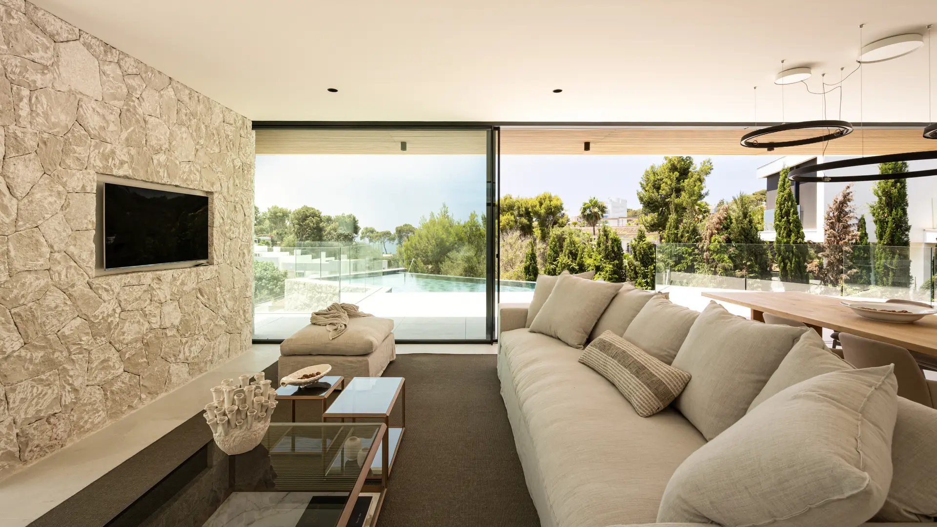 Luxury villa living room with natural stone walls, pool terrace and garden views in Bendinat, Mallorca — exclusive property represented by Isabella Janoschka